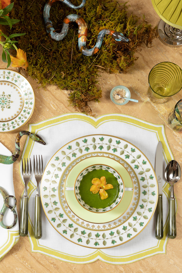 Close up photograph of a table setting featuring luxury china, flatware, linens, and glassware, along with ceramic snakes resting amongst live moss and fresh flowers.