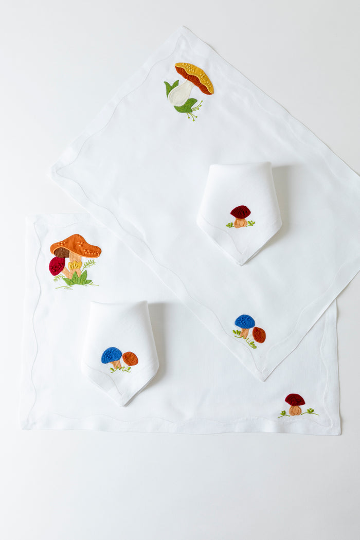 2 linen placemats with French stitch appliqué of mushrooms. Each placemat is 19" by 13". On top of each placemat is a cocktail napkin with French stitch appliqué of mushrooms.