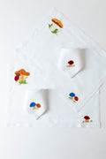 2 linen placemats with French stitch appliqué of mushrooms. Each placemat is 19" by 13". On top of each placemat is a cocktail napkin with French stitch appliqué of mushrooms.