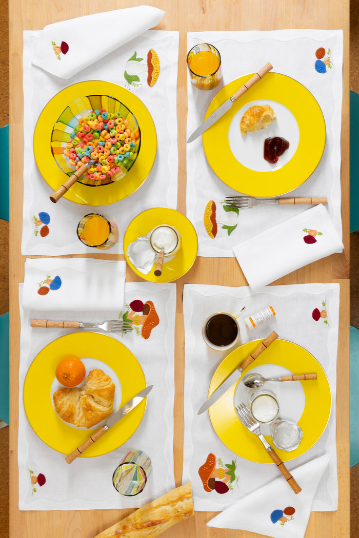 Photograph of a table setting featuring linen placemats with French stitch appliqué of mushrooms.